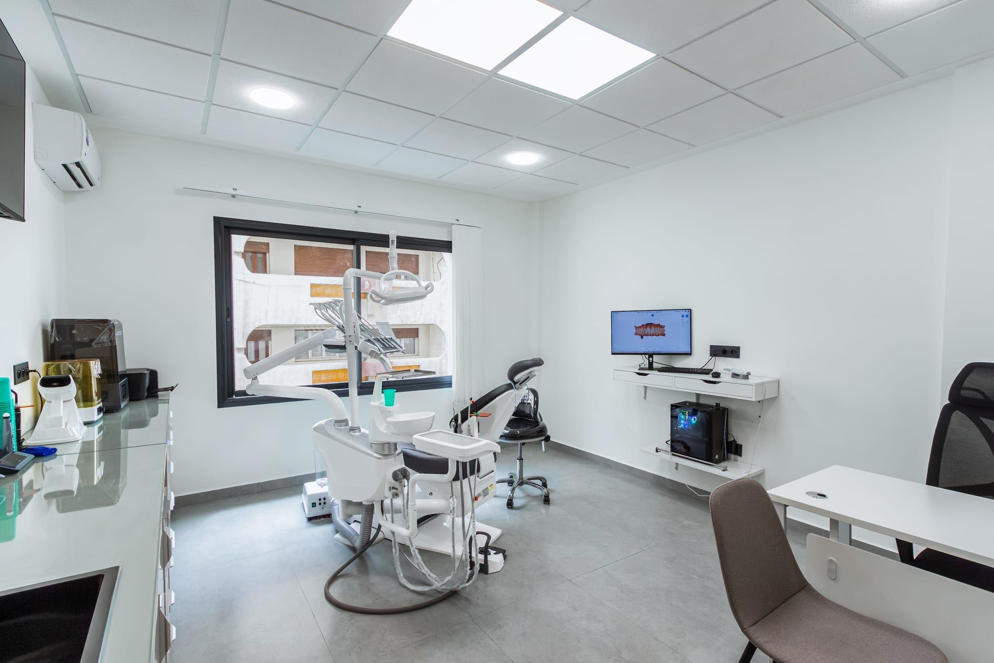 Salle de soins du cabinet, avec le fauteuil dentaire, la fenêtre et un écran au mur