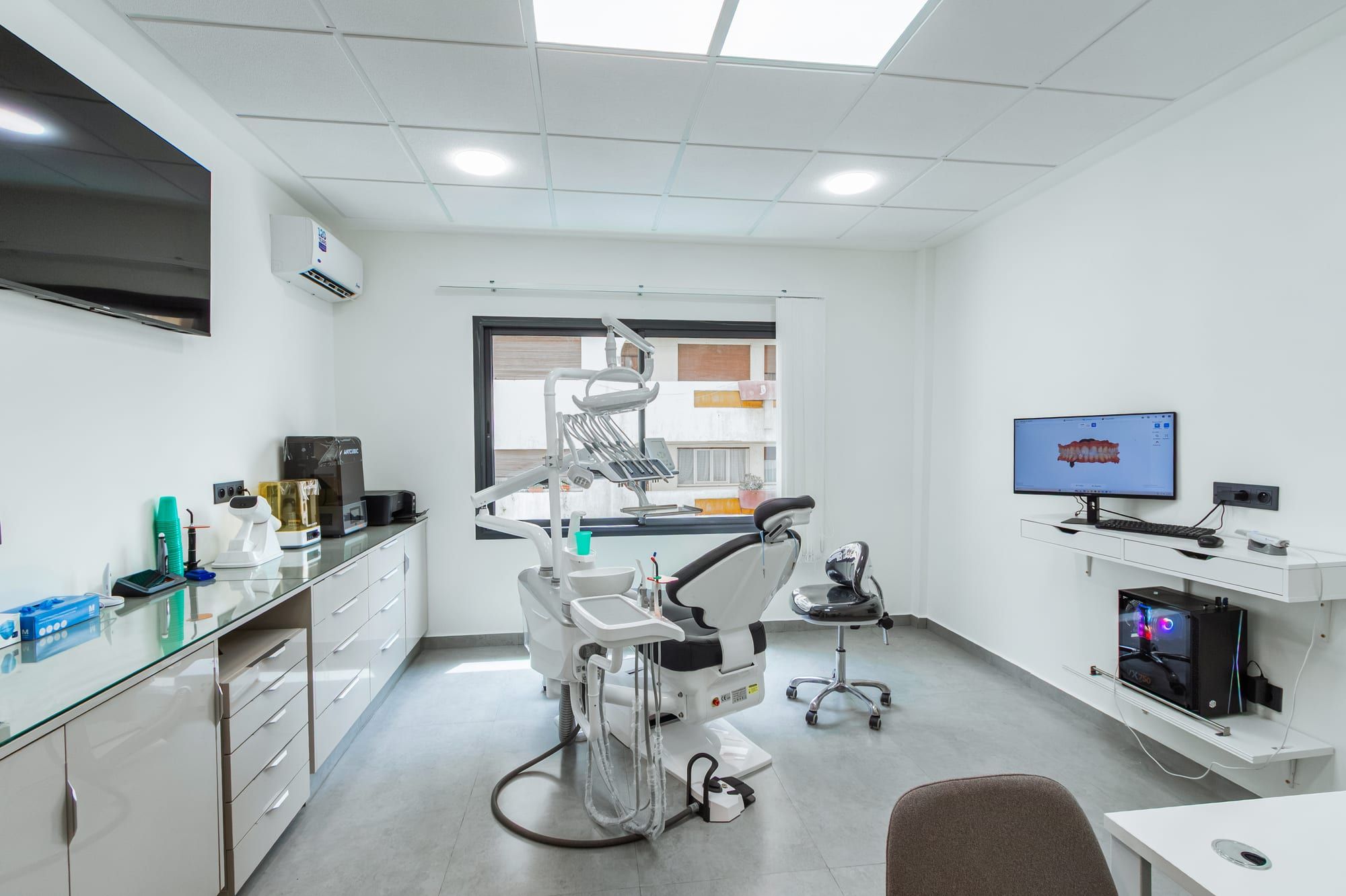 Salle de soins avec le fauteuil dentaire, le plan de travail et un écran